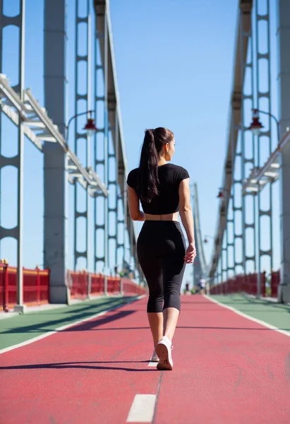 Pretty fitness woman wearing sport apparel walking at the bridge