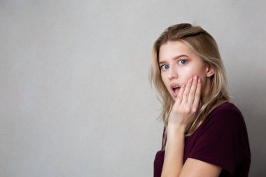 Gri bir arka üzerinde poz doğal makyaj ile korkmuş sarışın kadın