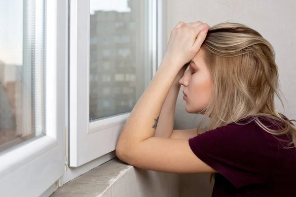 Traurige blonde Frau, die ihren Kopf mit den Händen bedeckt, sitzt in der Nähe des Sieges — Stockfoto