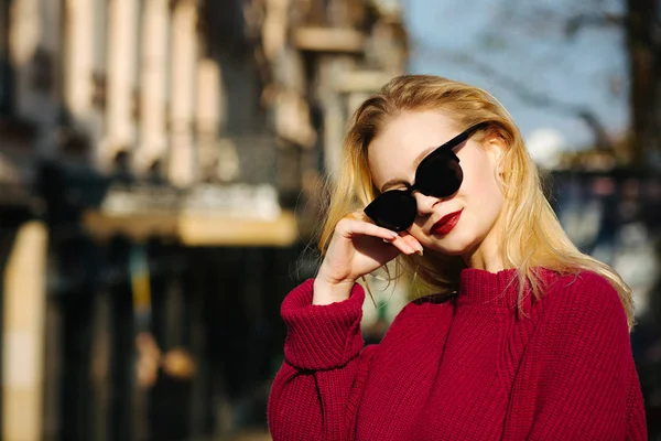 Glad tjej klädd i tröja och solglasögon poserar i staden. — Stockfoto