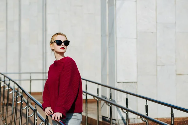 Elegante mujer rubia con suéter y gafas de sol caminando en t —  Fotos de Stock