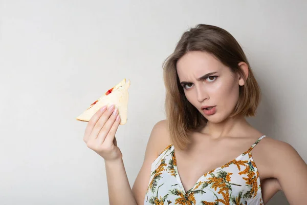 Boos brunette meisje student het eten van een sandwich over een grijze backgr — Stockfoto