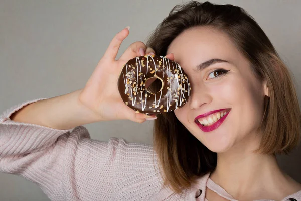 Cheerful flirty girl with natural makeup holding donut against a — Stock Photo, Image