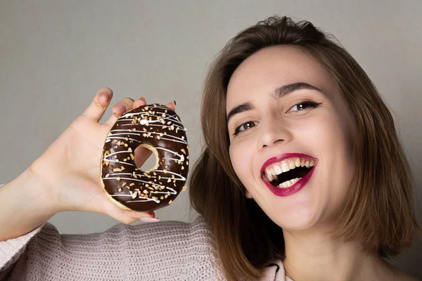 Pretty flirty girl with natural makeup holding donut against a g — Stock Photo, Image