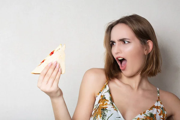 Gritando morena menina estudante comer um sanduíche sobre um cinza ba — Fotografia de Stock