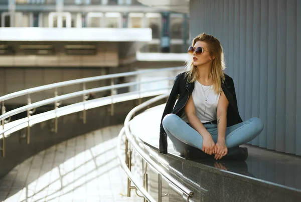 Fashionable stylish woman wearing jeans and jacket sitting on st — Stock Photo, Image