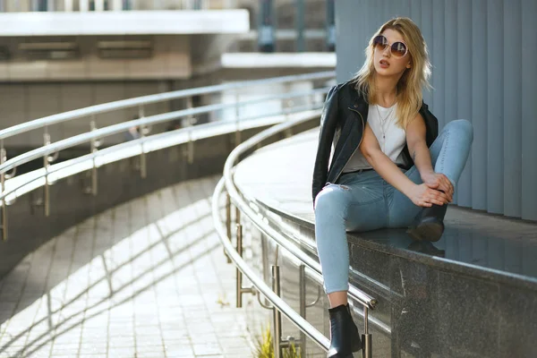 Schöne stylische Frau in Jeans und Jacke sitzt auf der Straße — Stockfoto