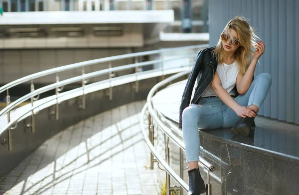 Stunning stylish woman wearing jeans and jacket sitting on stree — Stock Photo, Image