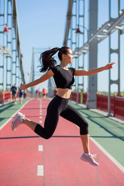 Deportiva chica morena saltando en la pista de jogging — Foto de Stock