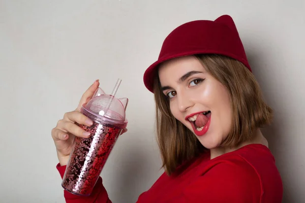 Flirty brunette woman in red hat holding cherry juice glass and — Stock Photo, Image