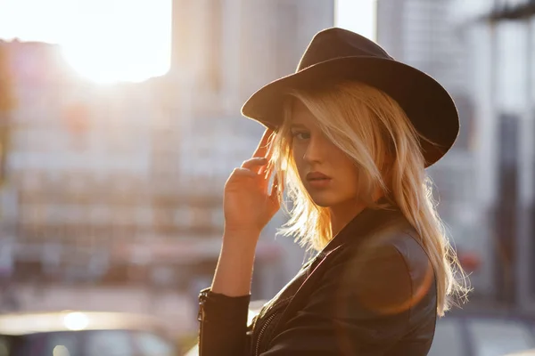 Stunning blonde woman wearing black hat posing at sunset with su — Stock Photo, Image
