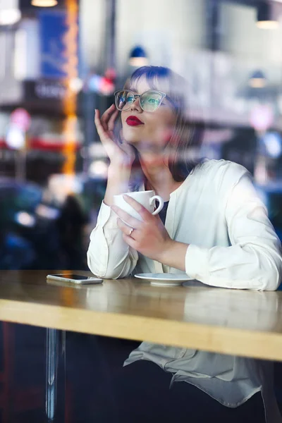 Charming young woman wearing glasses spending time in the restau