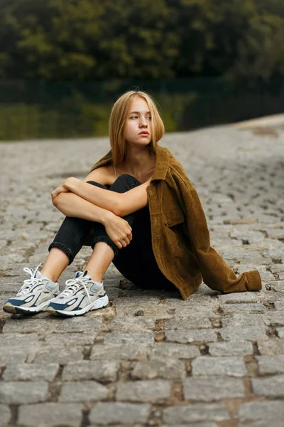 Sad young woman sitting on the road with paving stones