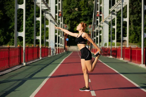 Sporty red haired woman doing stretching workout at the bridge. — Stock Photo, Image