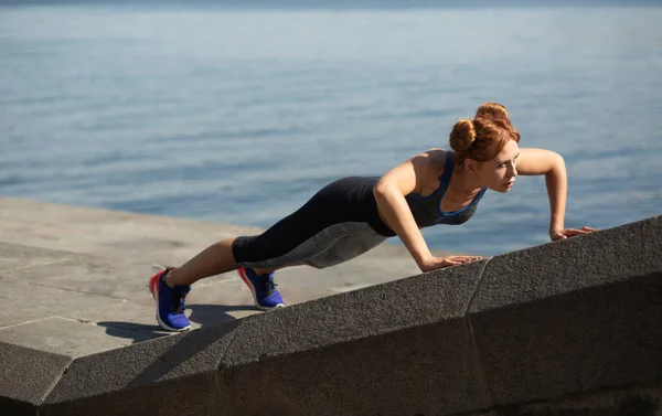 Full length side view of a pretty athletic woman doing push ups — Stock Photo, Image