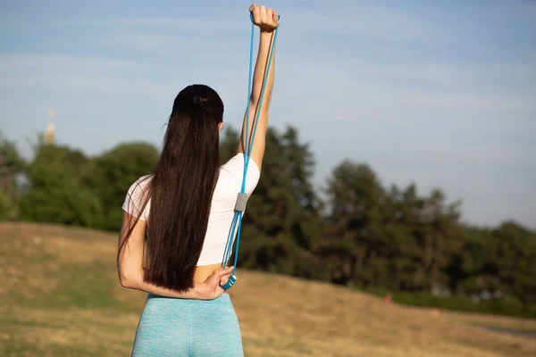 Стройная спортивная девушка делает упражнения на растяжку с резиновым сопротивлением — стоковое фото