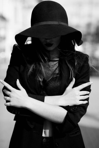 Elegant brunette woman wears lace bra, cap and suit posing at the city. Black and white shot