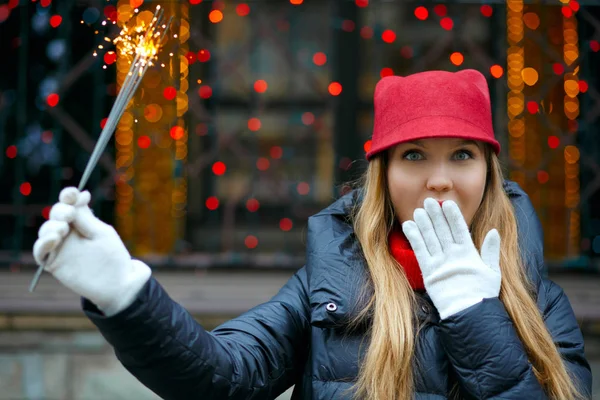 Şaşırmış kız elinde maytap tutan kırmızı bir şapka takıyor.