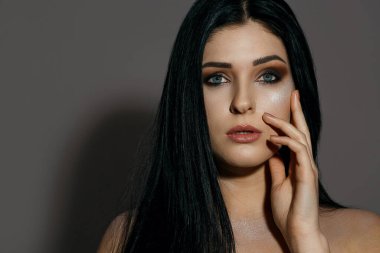 Kahverengi dumanlı göz makyajı ve parlayan cildiyle muhteşem esmer bir kadının stüdyo portresi. Stüdyo, gölgeli gri bir arka plan üzerine çekim yaptı. Metin için boşluk