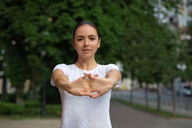 Esmer atletik kadın parkta esneme hareketleri yapıyor.