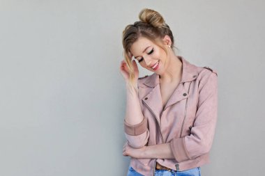 Neşeli genç bir kadının atölye çekimi açık pembe ceket giyiyor ve gri bir duvarın yanında duruyor. Boş boşluk