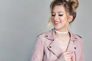 Zarif genç bir kadının stüdyo fotoğrafı açık pembe ceket giyiyor ve gri bir duvarın yanında duruyor. Boş boşluk