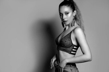 Seksi sarışın kız şık sütyen ve kot pantolon giyer. Stüdyo gri arka planda poz verir. Metin için boşluk