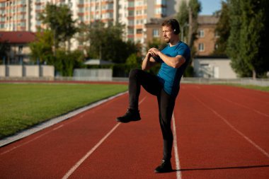 Spor kıyafetli genç bir sporcu antrenmandan önce ısınıyor ve kulaklıkla müzik dinliyor. Boş boşluk