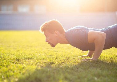 Atletik adam stadyumda şınav çekerken mavi tişört giyer. Boş boşluk