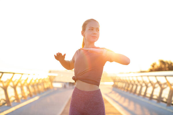 Adorable red haired teenage girl warming before workout at the bridge in rays of sun. Space for text