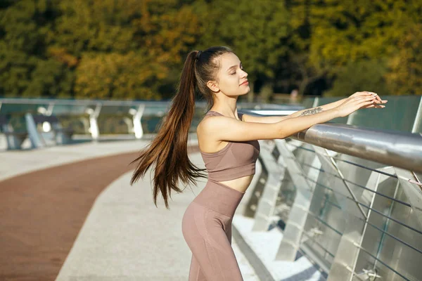 早上站在桥边的是身材苗条的女运动员 身上有刺青和长长的闪亮的头发 空旷的空间 — 图库照片