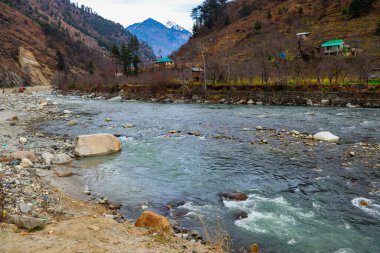 Yol kenarından akan bir nehir ve dağda nehirde kayalar var.
