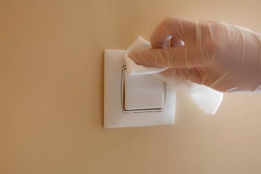 Eldivenlerle ışık düğmesini silen ve yüzeyi Covid-19 virüsünden arındırmak için dezenfektan kullanan kadın.