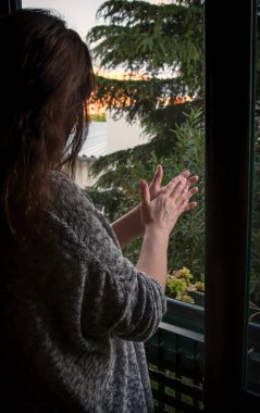 Coronavirus hapsi sırasındaki sağlık personeline ve diğer gruplara şükranlarını sunmak için penceresinde alkışlayan kadın.