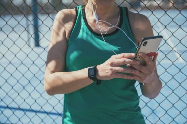 Çitin üstünde akıllı telefonunu kullanan tanınmayan bir sporcu kadın.