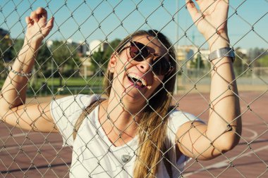 Modern Kadın Gülüşü. Genç kadın basketbol çitlerine gülüyor. Beyaz giyinmiş ve güneş gözlüğü takan komik bir kadın. Yaşam biçimi