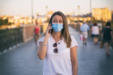 Yüzü Maskeli Kadın Telefonu Kullanıyor. Covid-19 yüzünden caddelerde koruyucu maske takarak yürüyen çekici bir kadın. Telefonunu kullanıyor..