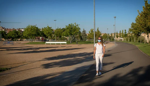 Woman with protective mask on the street.Attractive woman walking through a lonely park wearing a protective mask due to covid-19.