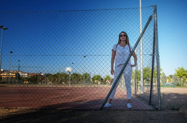 Modern Woman Laughing.Young woman laughing against basketball fence. Funny woman dressed in white and wearing sunglasses. Lifestyle