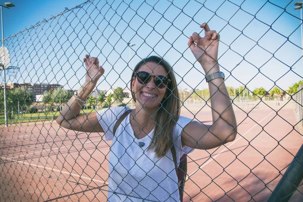 Modern Woman Laughing.Young woman laughing against basketball fence. Funny woman dressed in white and wearing sunglasses. Lifestyle