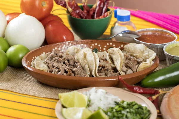 Typical Mexican food dishes with sauces on colorful table. Tacos of roasted meat in clay dish.