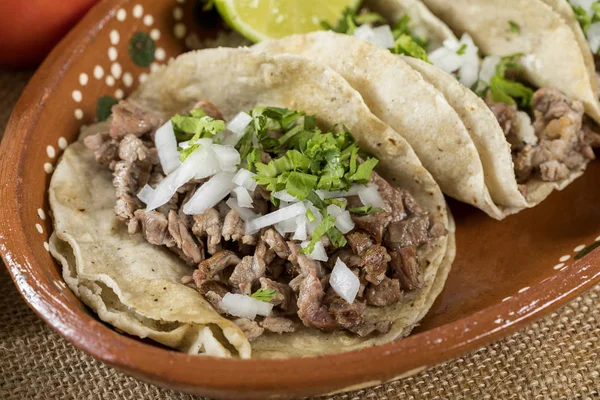 Typical Mexican food dishes with sauces on colorful table. Tacos of roasted meat in clay dish.