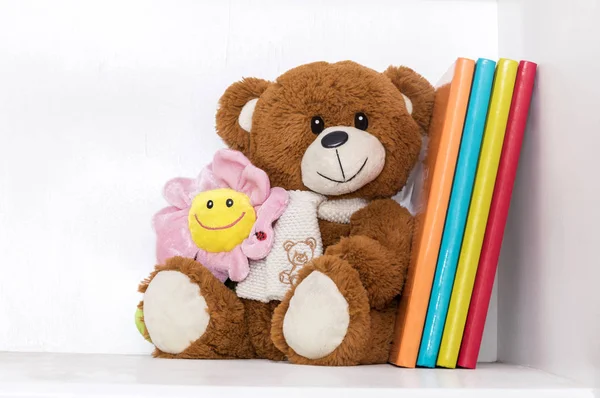 Teddy bear soft toy in child\'s bedroom with colorful books and pink flower