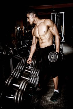 Spor salonunda egzersiz yaparak genç kaslı adam. Kaslarına gösterilen.