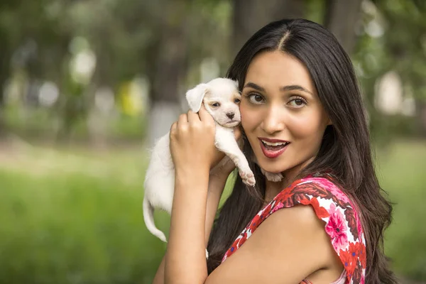 Beautiful young latin woman in the park with a small white puppy in her hands.