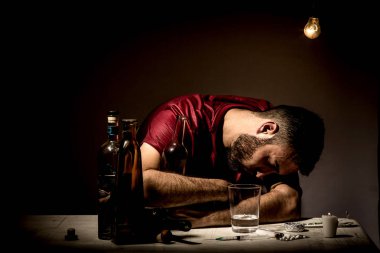 Sakallı genç adam, alkolizm, sigara ve uyuşturucu bağımlılığında kaybolmuş.