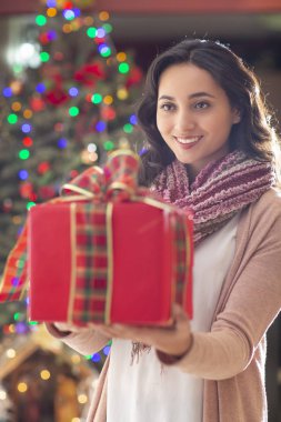 Kırmızı hediye ve Noel ağacı içinde belgili tanımlık geçmiş ile gülümseyen genç güzel latin kadın portresi