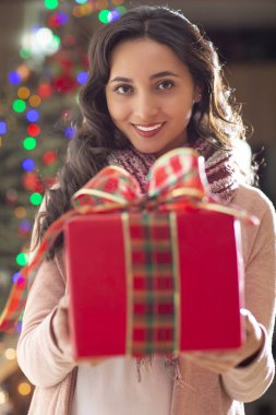 Kırmızı hediye ve Noel ağacı içinde belgili tanımlık geçmiş ile gülümseyen genç güzel latin kadın portresi