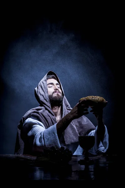 Jesus Christ praying to God consecration the bread and grapes in the dark black night.