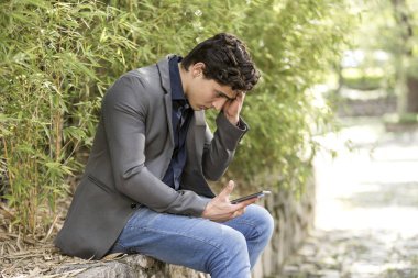 Elinde cep telefonu ile bahçede oturan genç sorunlu iş adamı.